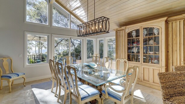 Un coin repas avec une table en verre entourée de chaises, de grandes fenêtres et un buffet en bois doté de portes en verre.