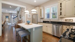 Een moderne keuken met een centraal kookeiland, roestvrijstalen apparatuur en een eetgedeelte met barstoelen.