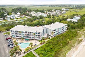 A multi-story hotel with a swimming pool, surrounded by lush greenery and a beach. - Bay View Villas 106 | Waterfront, Community Pool (Tybee Island)