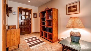 A hallway with a wooden door, a bookshelf, a lamp, and a patterned rug. - A Downtown Breck Oasis. Enjoy Convenience with Onsite Pool sh15 (Breckenridge)