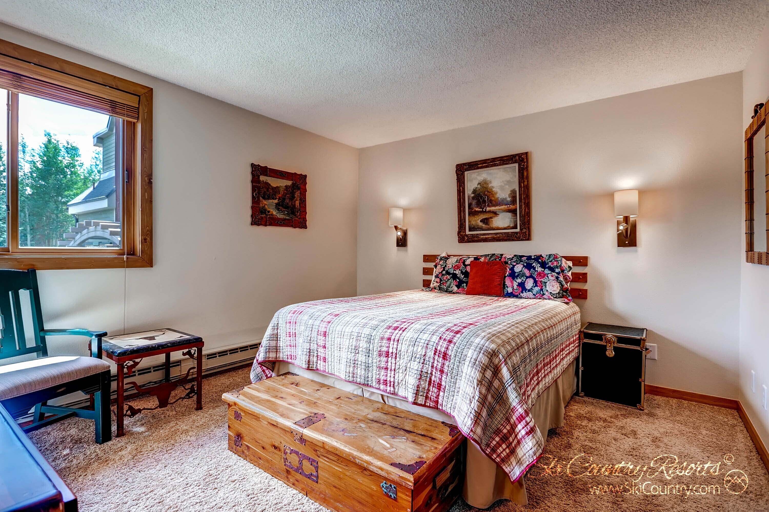 Une chambre à coucher comprenant un lit, un bureau, une chaise, une commode en bois et deux lampes fixées au mur.