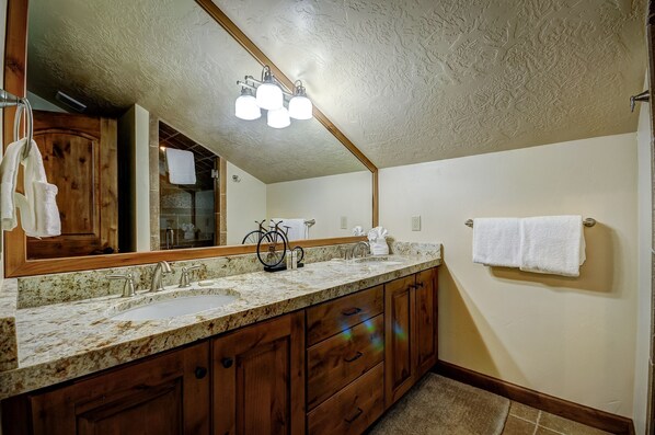 A bathroom with a double sink, wooden cabinets, a large mirror, and a ceiling light fixture.