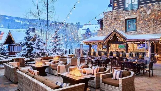 An outdoor seating area with wicker furniture and a fire pit, set against a stone building with a bar and a mountain view. - Ritz Carlton 1BR Ski-in/out - 2 Queen Beds - Sleeps 4 (Beaver Creek)