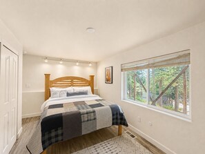 A bedroom with a wooden headboard, a large window with a view of trees, a quilt on the bed, and a white door.