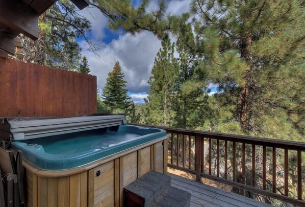 Relax on the deck with a hot tub, surrounded by a fence and serene pine trees.