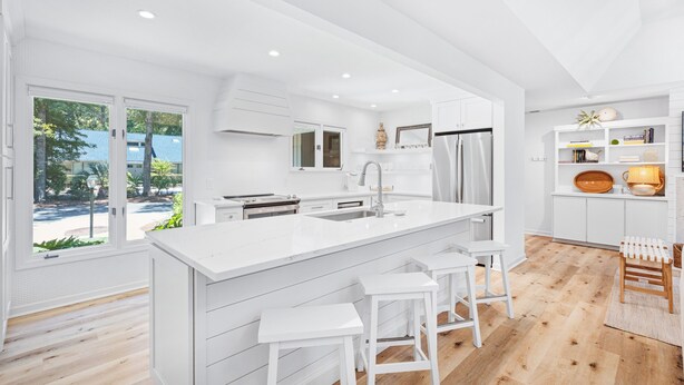 A modern kitchen with a large island, white cabinetry, and a view of the outdoors.