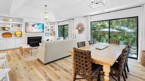 A spacious living area with a wooden dining table, wicker chairs, a sofa, and a fireplace.