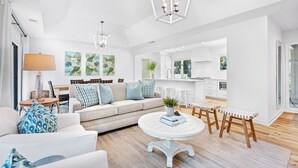 A modern living room with a sofa, coffee table, and wooden stools. A kitchen is visible in the background.