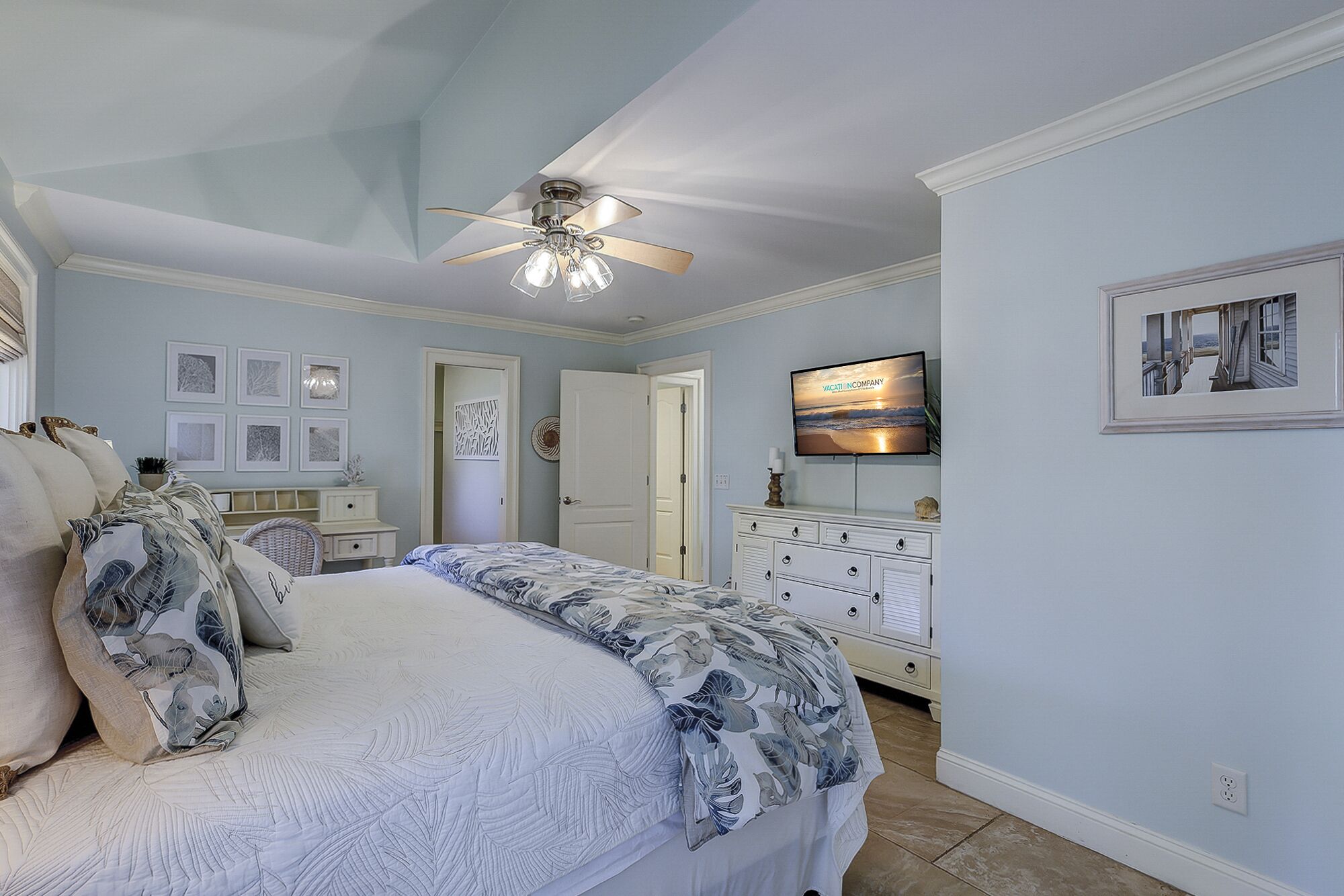A bedroom with a bed, a ceiling fan, a dresser, a television, and framed pictures on the wall.