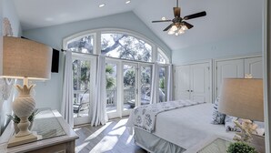 A bedroom with a large window, a ceiling fan, and a bed with a patterned bedspread. - 106 Oceanwood Trace - 2nd Row Ocean View, Dog Friendly Beachside Oasis. (Hilton Head Island)