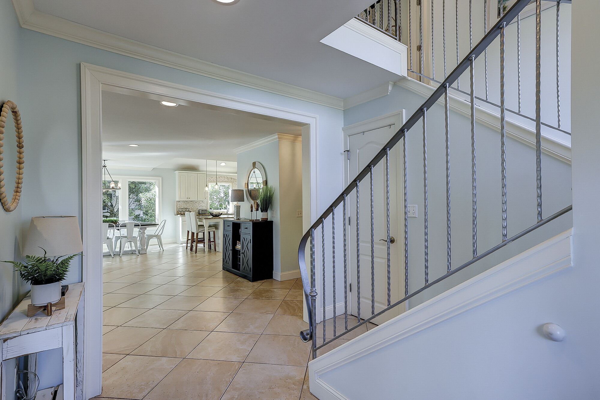 A staircase with a metal railing leading to a second floor. A dining area with white chairs and a table is visible in the background.