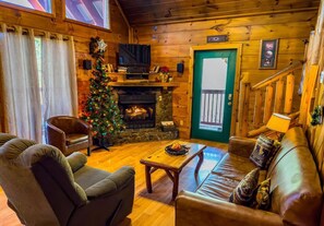 A cozy log cabin interior with a fireplace, a Christmas tree, leather furniture, and a television. - Privacy~Sunset View~Pet Friendly~Pool Table~Air Hockey (SEVIERVILLE)