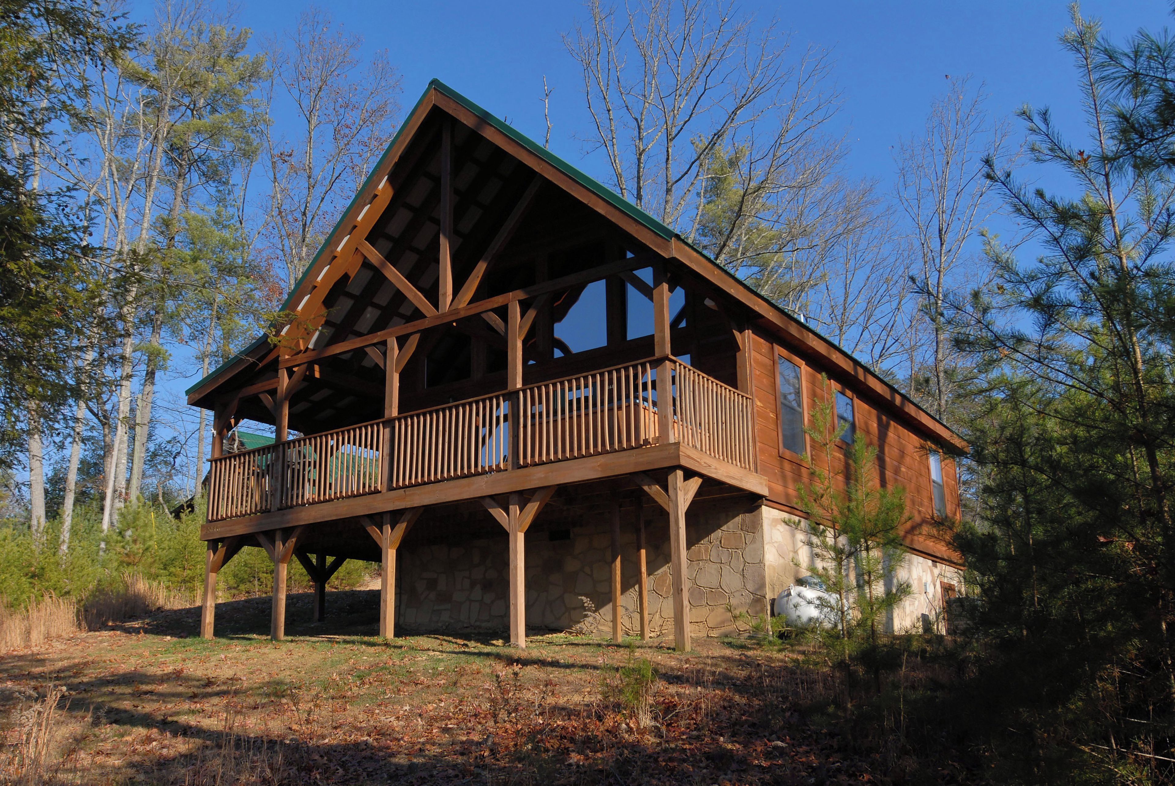 A cabin with a balcony, stone foundation, and surrounded by trees.