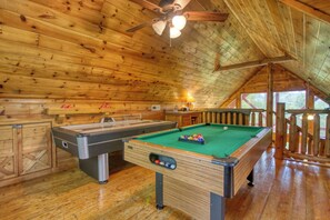 A wooden interior with a pool table, a billiards table, and a ceiling fan.