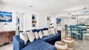 Un salon moderne avec un canapé bleu, un coin repas avec des chaises turquoise et une cuisine en arrière-plan.