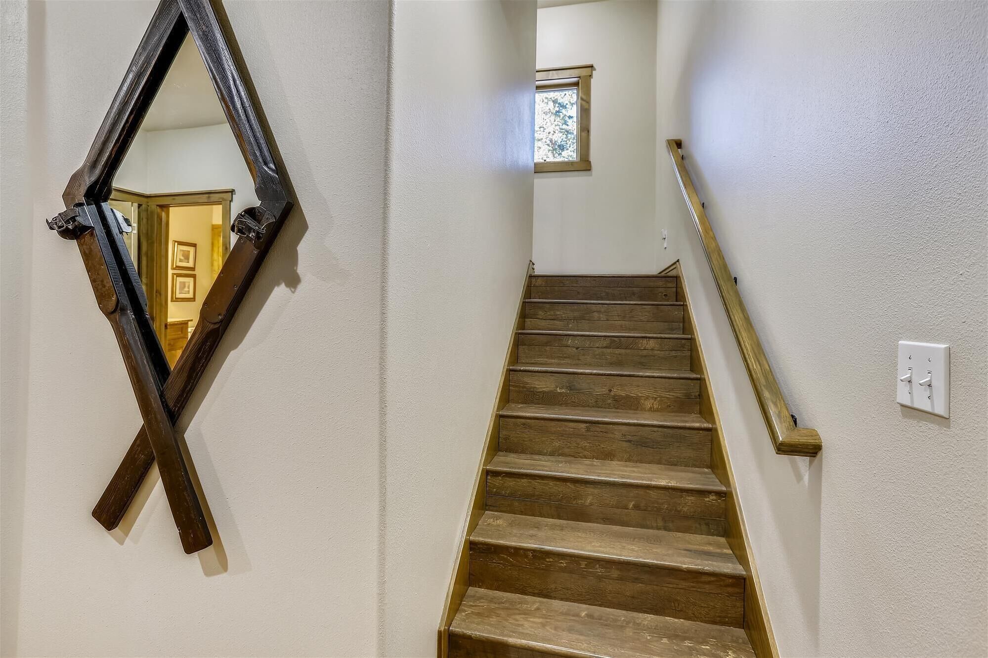 Eine Holztreppe mit Handlauf, ein Wandspiegel und ein Fenster mit Blick in einen anderen Raum.