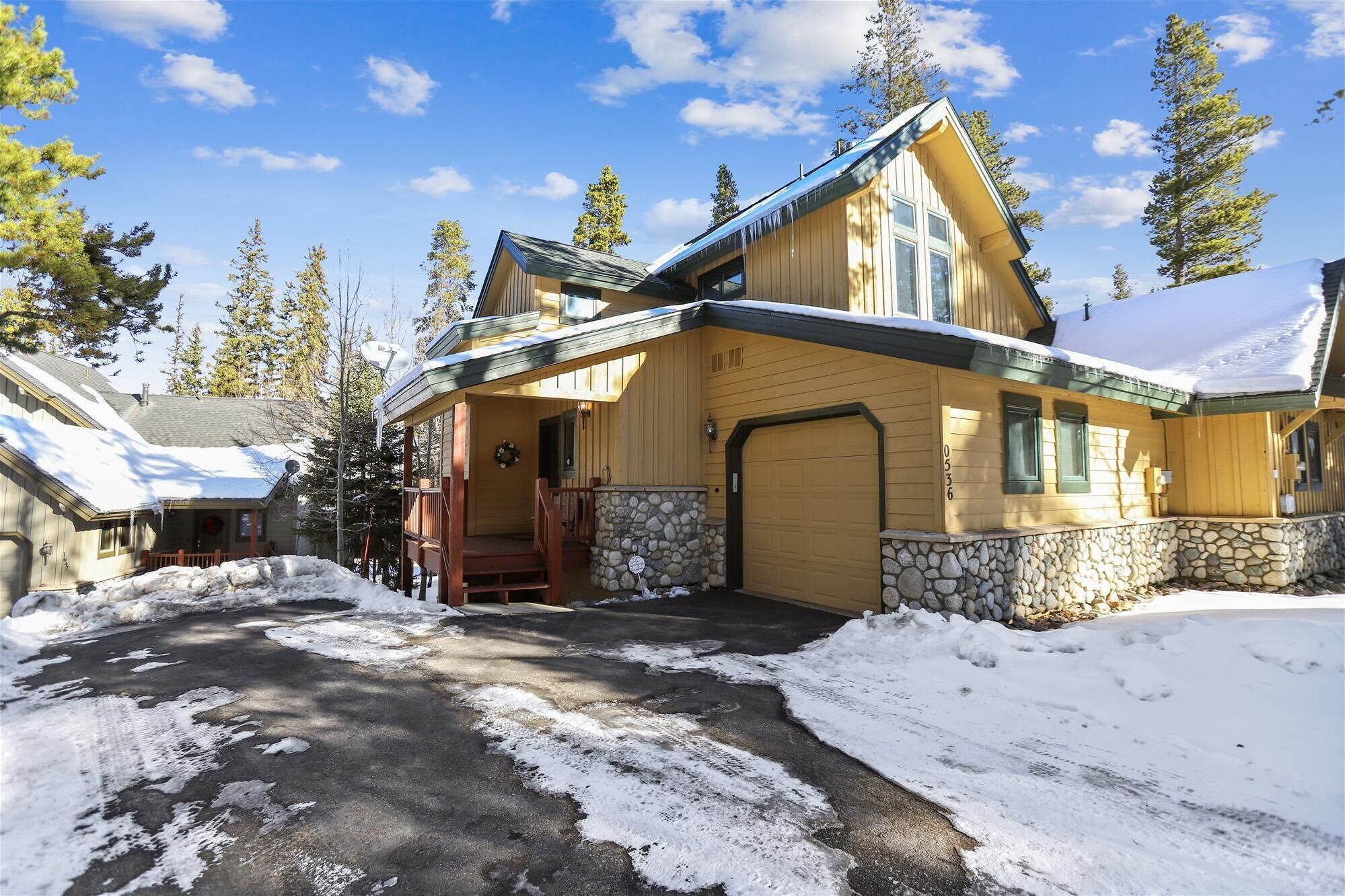 A wooden lodge with a stone foundation, a covered porch, and a garage.