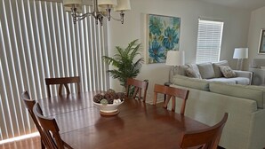 A dining area with a wooden table, chairs, and a bowl of decorative items. There is a sofa and a painting on the wall. - Amazing Location & Beautiful home with Golf Cart, BBQ & WiFi included! (The Villages)