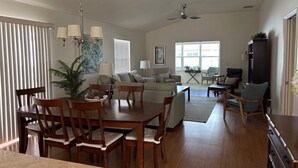 A spacious living room with a dining area, a ceiling fan, and a large window providing natural light. - Amazing Location & Beautiful home with Golf Cart, BBQ & WiFi included! (The Villages)
