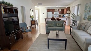 A living room with a TV, sofa, coffee table, and a dining area with a table and chairs. - Amazing Location & Beautiful home with Golf Cart, BBQ & WiFi included! (The Villages)
