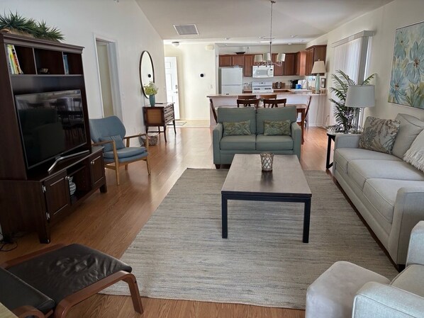 A living room with a TV, sofa, coffee table, and a dining area with a table and chairs. - Amazing Location & Beautiful home with Golf Cart, BBQ & WiFi included! (The Villages)