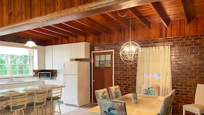 Una cocina rústica con gabinetes blancos, un refrigerador y una zona de comedor con una mesa y sillas de madera.