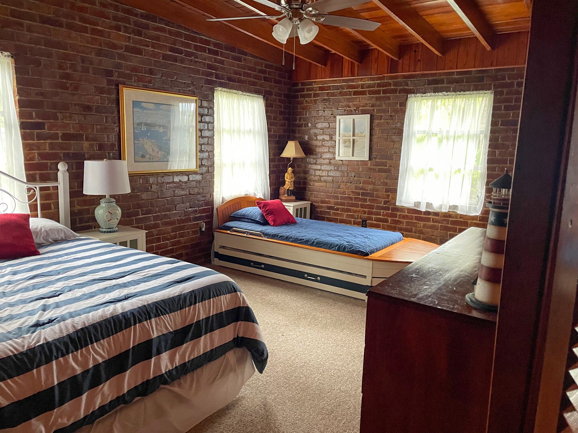 Un dormitorio acogedor con pared de ladrillo, dos camas, un ventilador de techo y una mesita de noche con lámpara.