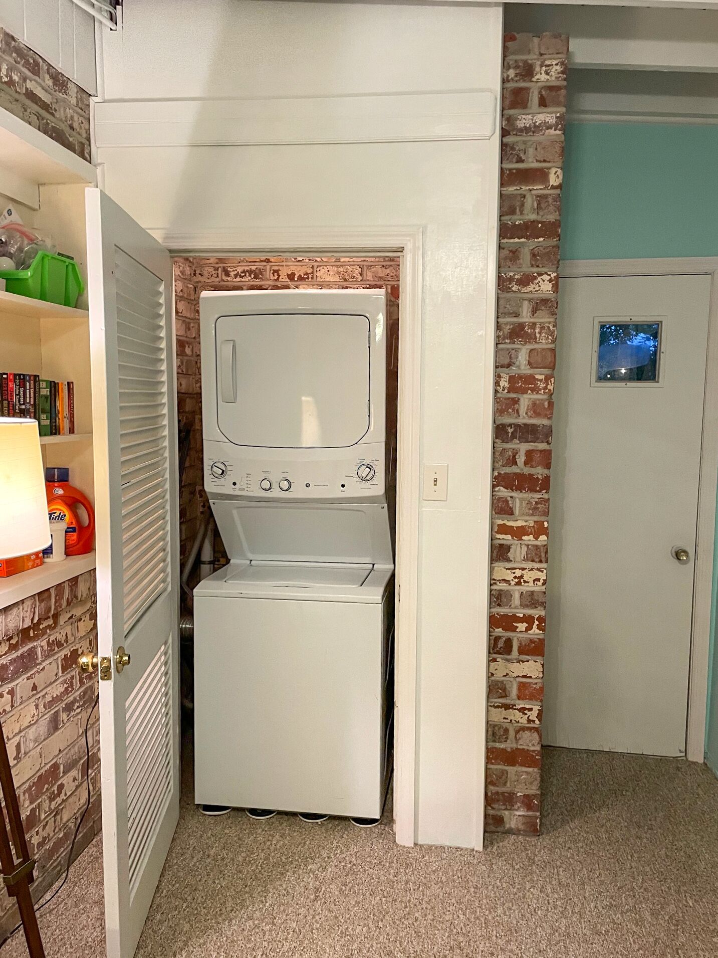 A compact laundry room with a washer and dryer, a bookshelf with books, and a door with a small window.