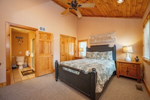 A bedroom with a wooden ceiling fan, a bed with a floral bedspread, a nightstand with a lamp, and a painting on the wall. - Hidden Retreat w/ Hot Tub & Scenic Views (McHenry)