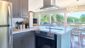 A modern kitchen with a central island, stainless steel appliances, and a view to an outdoor deck. - HOT TUB, Game Room, Walk to Beach, Fenced Yard, Dogs Ok (45th) (Long Beach)