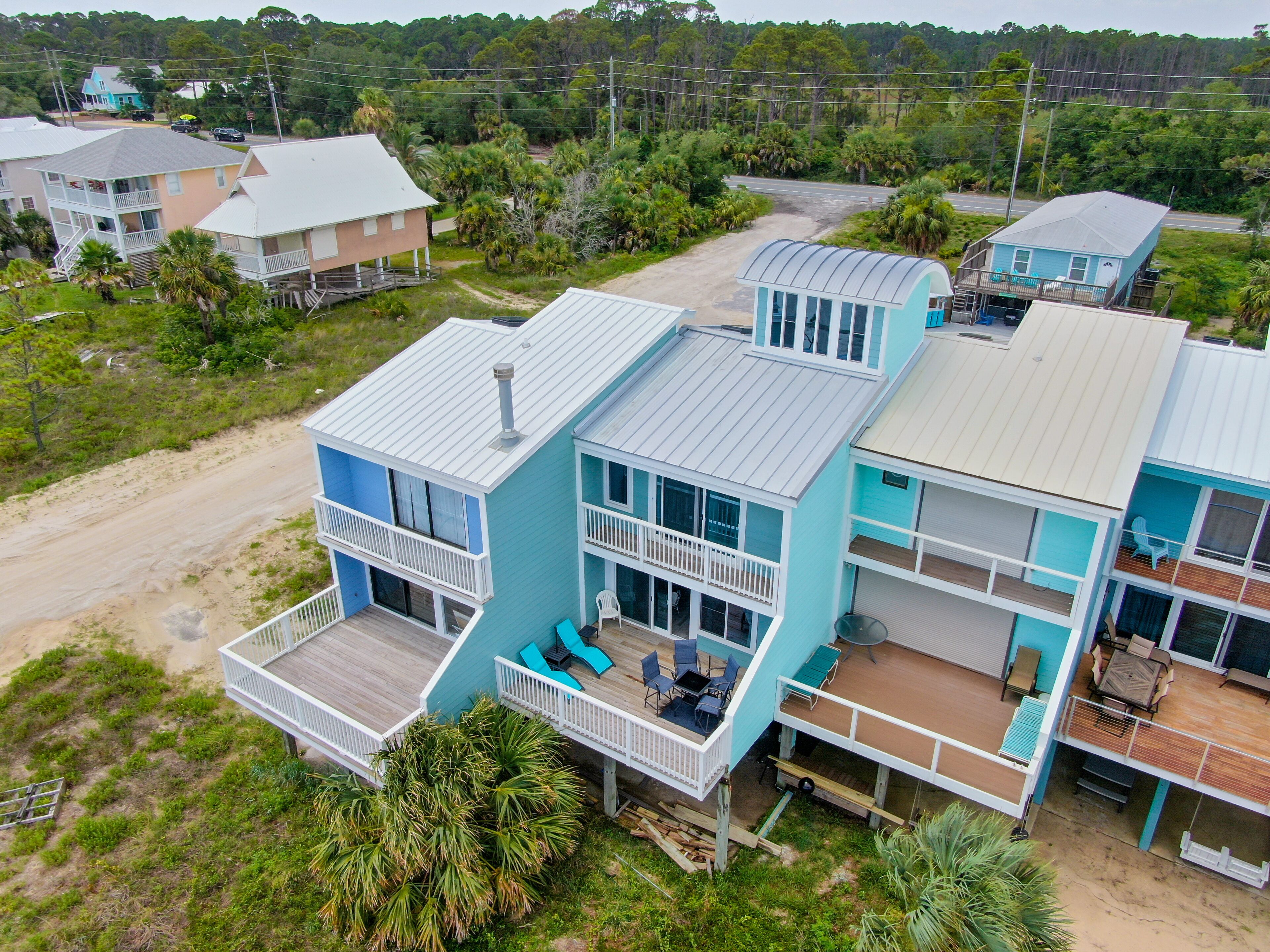 A multi-story beachfront property with balconies, outdoor seating, and a sandy driveway.