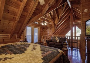 A log cabin interior with a large bed, a sofa, and a ceiling fan. - Pigeon Forge | Pet Friendly | Mountain Views | Hot Tub | Fireplace | WiFi (Pigeon Forge)