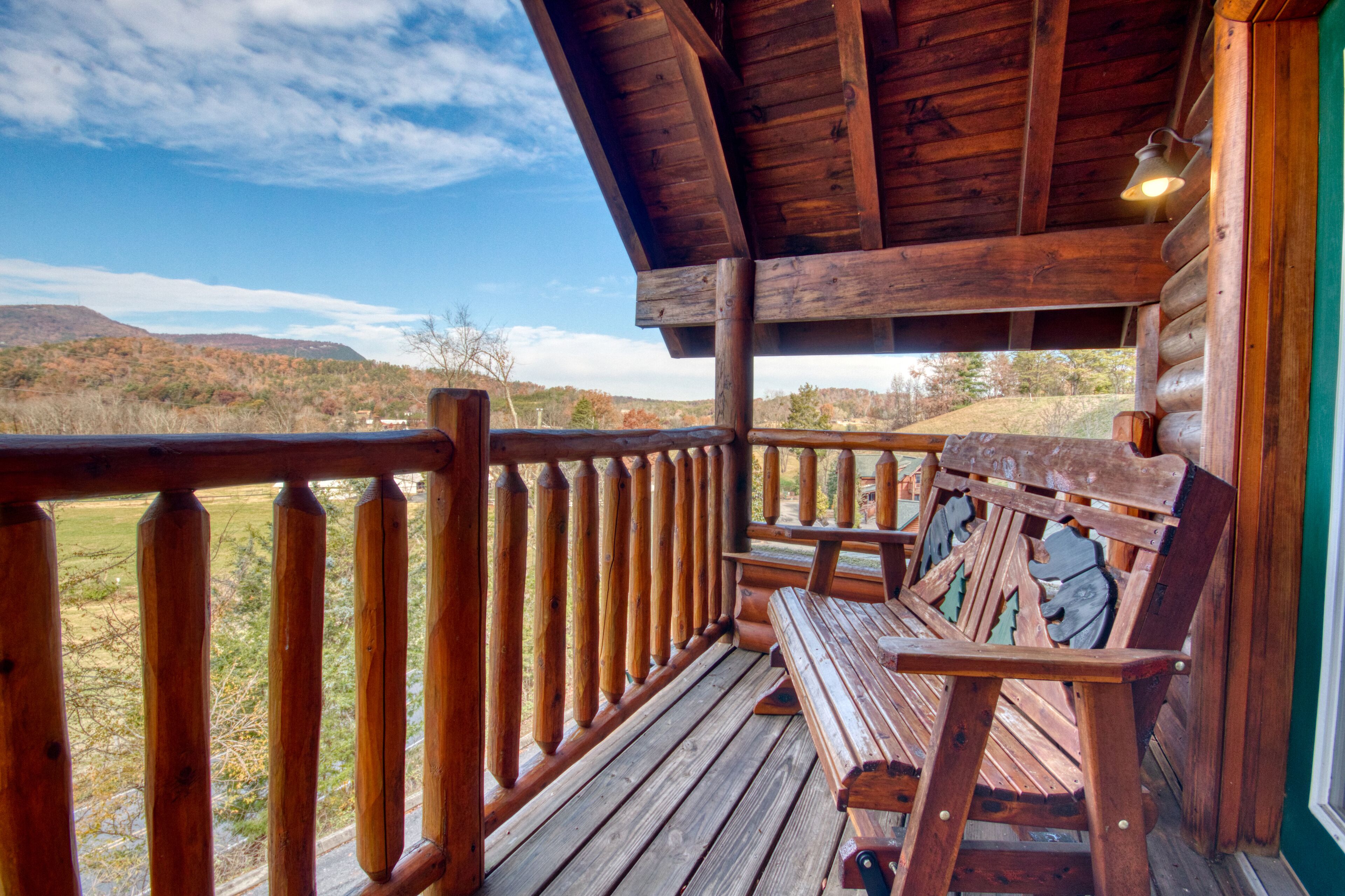A wooden deck with a bench, a railing, and a view of a hilly landscape.