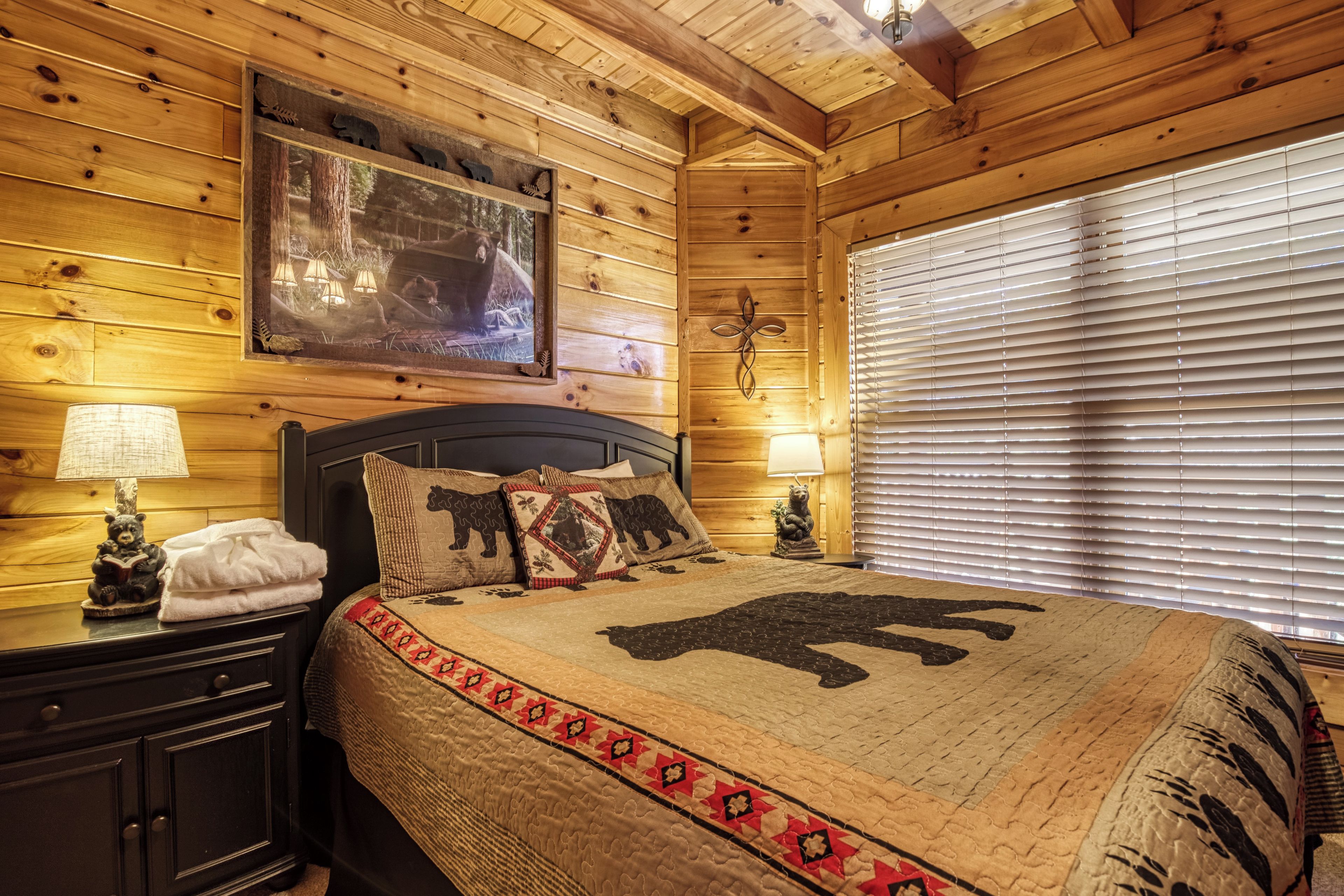 Une chambre de style cabane en bois, avec un lit, des tables de chevet et une fenêtre équipée de stores.