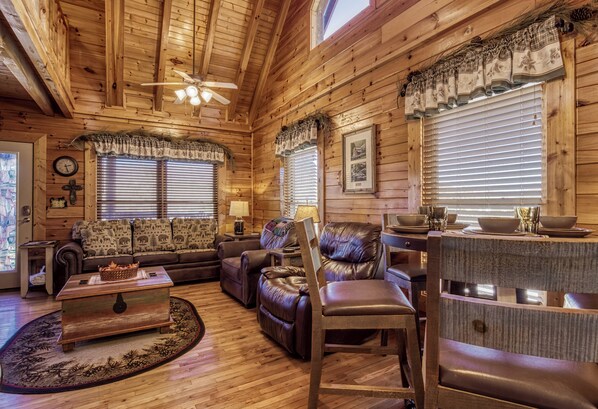A cozy cabin interior with wooden walls, a fireplace, a dining area, and a living room furnished with leather sofas and a coffee table. - Pigeon Forge | Pet Friendly | Mountain Views | Hot Tub | Fireplace | WiFi (Pigeon Forge)