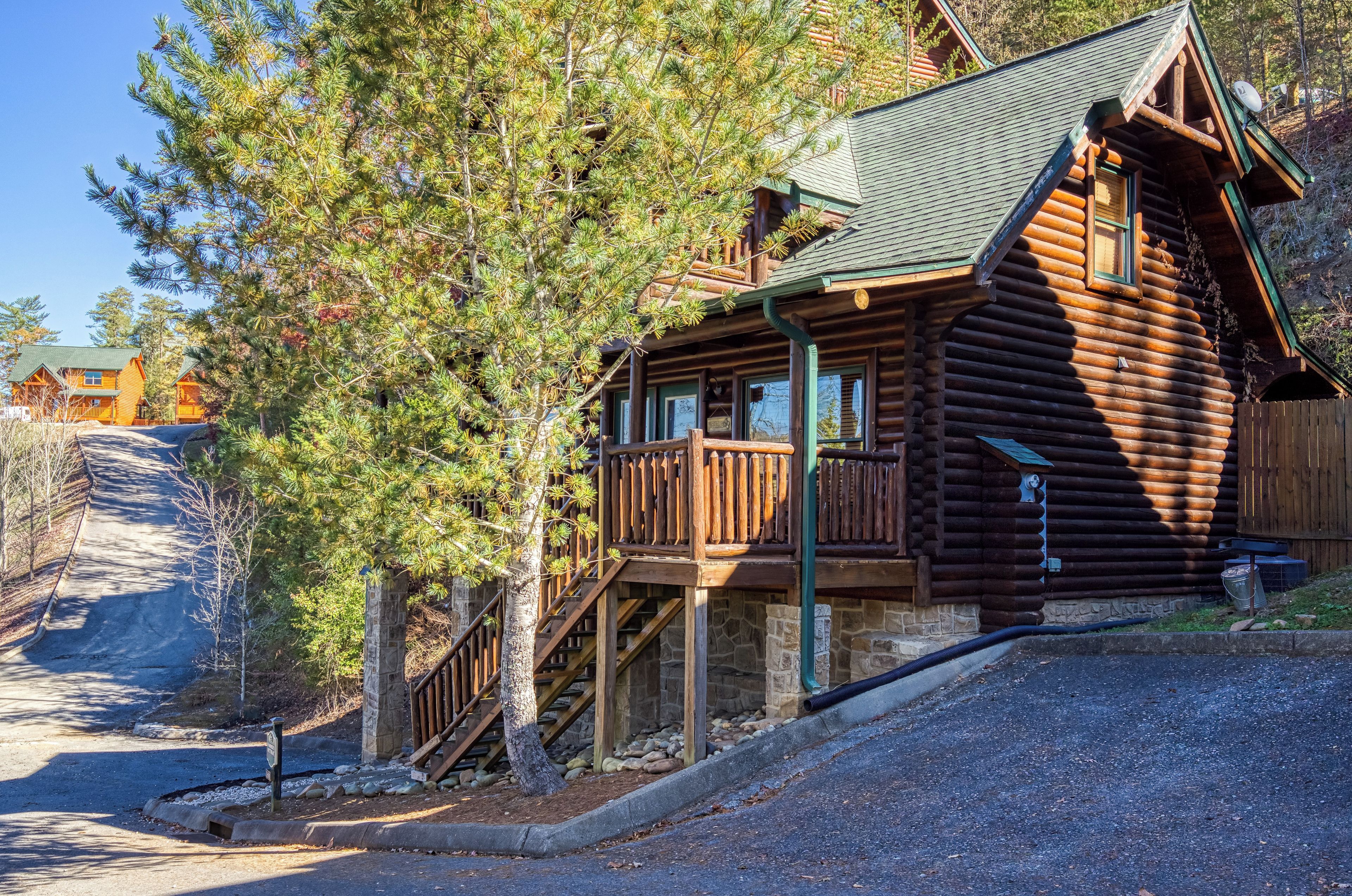 A log cabin with a wooden deck, stone foundation, and a staircase leading to the entrance.
