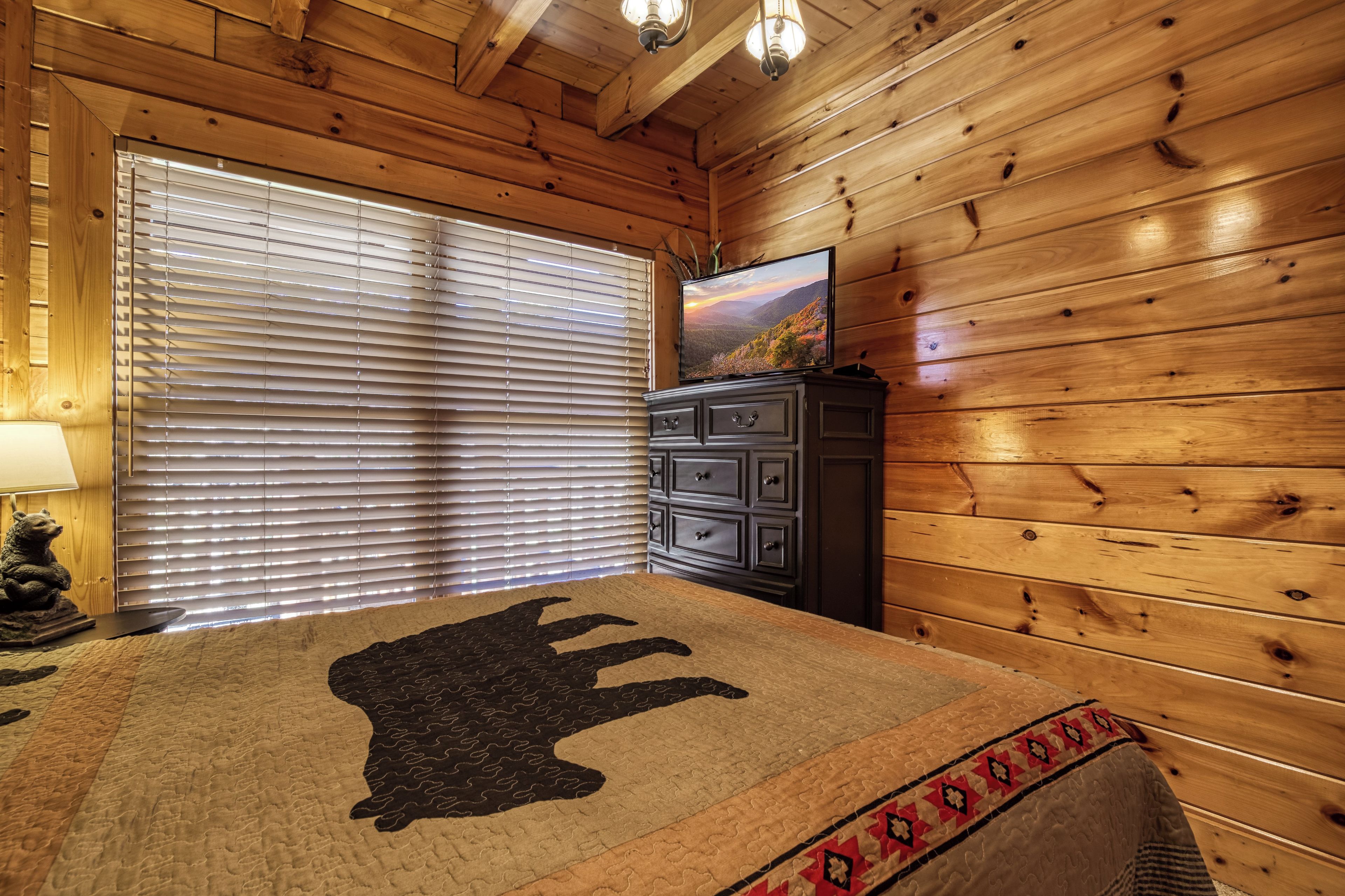 A wooden cabin room with a bed, a dresser, and a television on the wall.