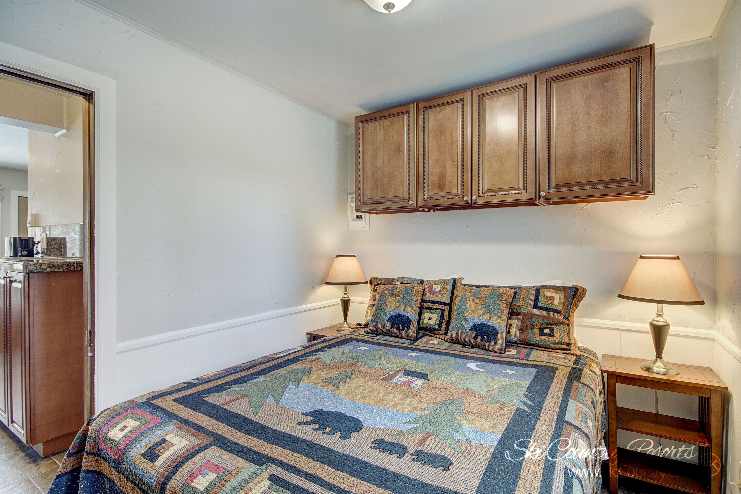 A bedroom with a large bed, two bedside lamps, a wooden wardrobe, and a nightstand with a lamp.