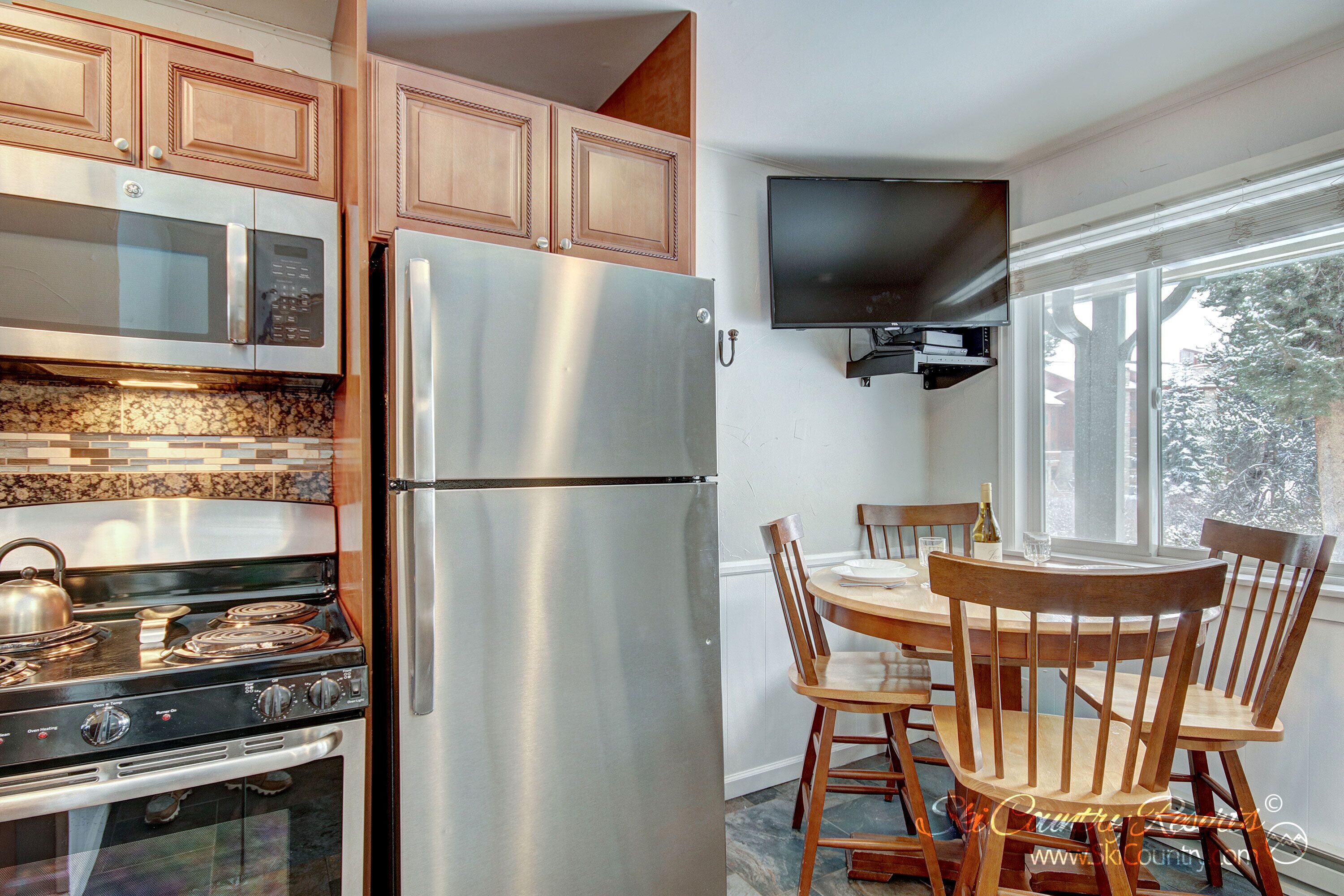 A modern kitchen with stainless steel appliances, wooden cabinets, and a dining area with a table and chairs.