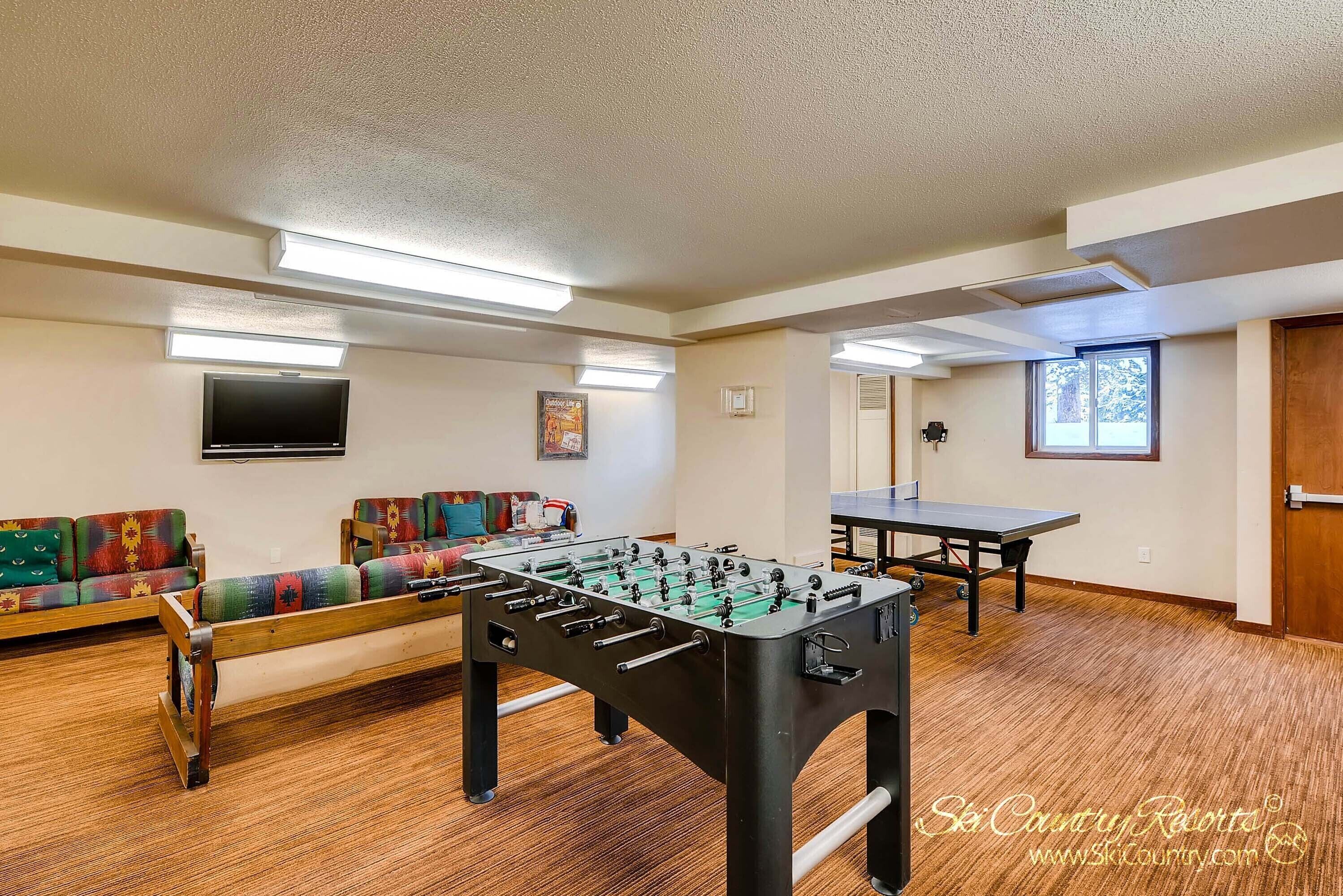 A room with a foosball table, a sofa, and a ping pong table.