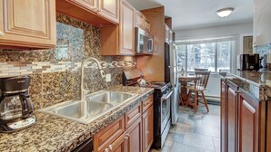 A kitchen with granite countertops, wooden cabinets, stainless steel appliances, and a large window providing natural light. - Stunningly Appointed Condo, Adjacent to Slopes/Hiking. Walk Downtown | PM2C (Breckenridge)
