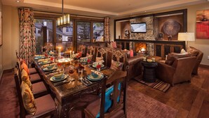 Un comedor con una larga mesa de madera dispuesta para una comida, rodeado de sofás de cuero y una chimenea.