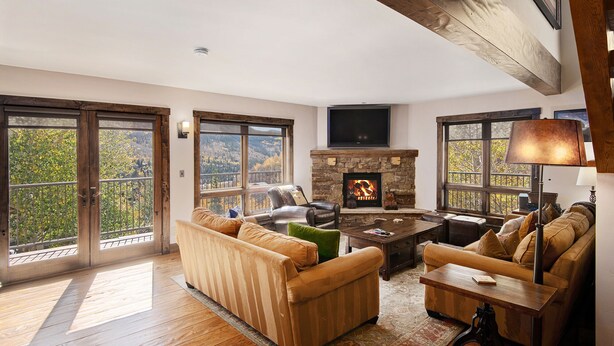A spacious living room with a stone fireplace, leather sofas, and large windows offering a view of the outdoors. - Airy Townhome in Vail w/ Beautiful Views, Modern Decor, Short Drive to Slopes (Vail)