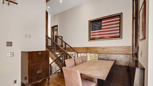 A dining area with a wooden table and bench, a staircase, and an American flag on the wall. - Airy Townhome in Vail w/ Beautiful Views, Modern Decor, Short Drive to Slopes (Vail)