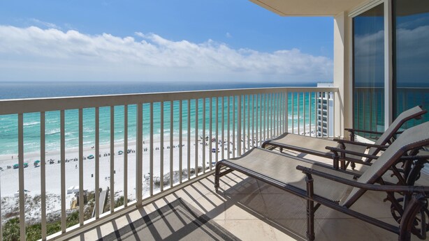 A balcony with a view of the beach and ocean. There are lounge chairs and a railing.