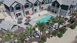 A multi-story hotel with a swimming pool, outdoor seating, and palm trees. - Pet-Friendly Beach Escape | Heated Pool & Private Patio (Corpus Christi)