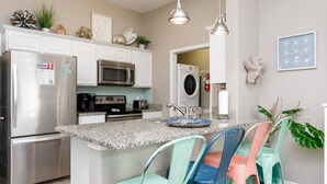 A modern kitchen with stainless steel appliances, a granite countertop, and colorful bar stools. - Pet-Friendly Beach Escape | Heated Pool & Private Patio (Corpus Christi)
