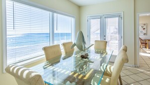 A dining area with a glass table, beige chairs, and a view of the ocean through large windows. - Gulf Front Condo, Elevator, Near Shops and Restaurants-Dune Allen Beach (Santa Rosa Beach)