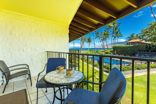 A balcony with a table and chairs, overlooking a pool and palm trees.