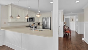 A modern kitchen with white cabinetry, stainless steel appliances, and pendant lighting. - C Street A - Incredible Ocean Front Condo in the heart of Wrightsville Beach (Wrightsville Beach)
